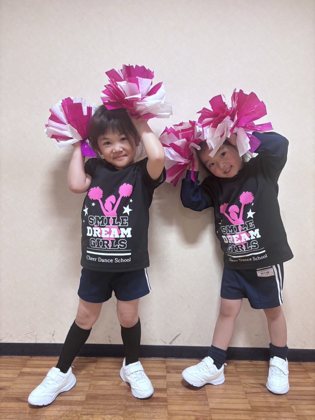 スマイルドリームガールズのTシャツを着て、ピンクのポンポンを持つ2人の女の子